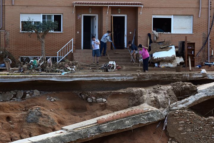 People try to clean the entrance of a building on October 31, 2024 in front of a street destroyed by the flash floods that have ravaged the town of Paiporta, in Valencia, eastern Spain. (Photo by JOSE JORDAN / AFP) (Photo by JOSE JORDAN/AFP via Getty Images)